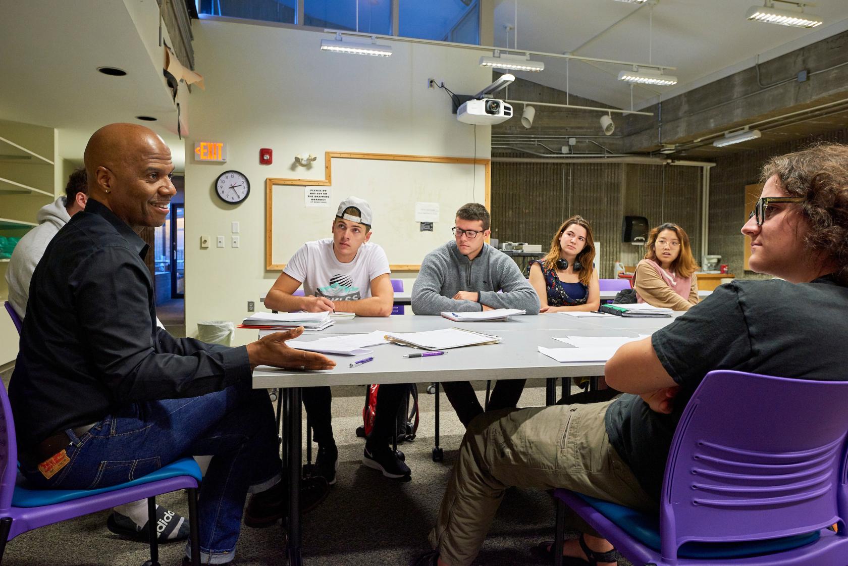 Professor sits with students and leads a discussion.