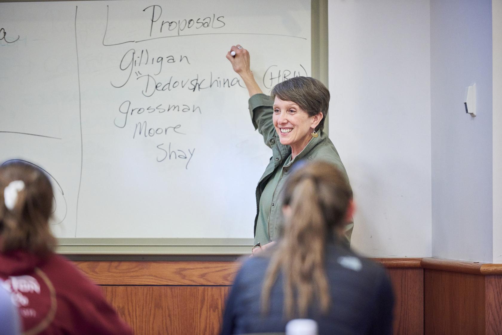 Professor writes on a whiteboard while addressing classroom
