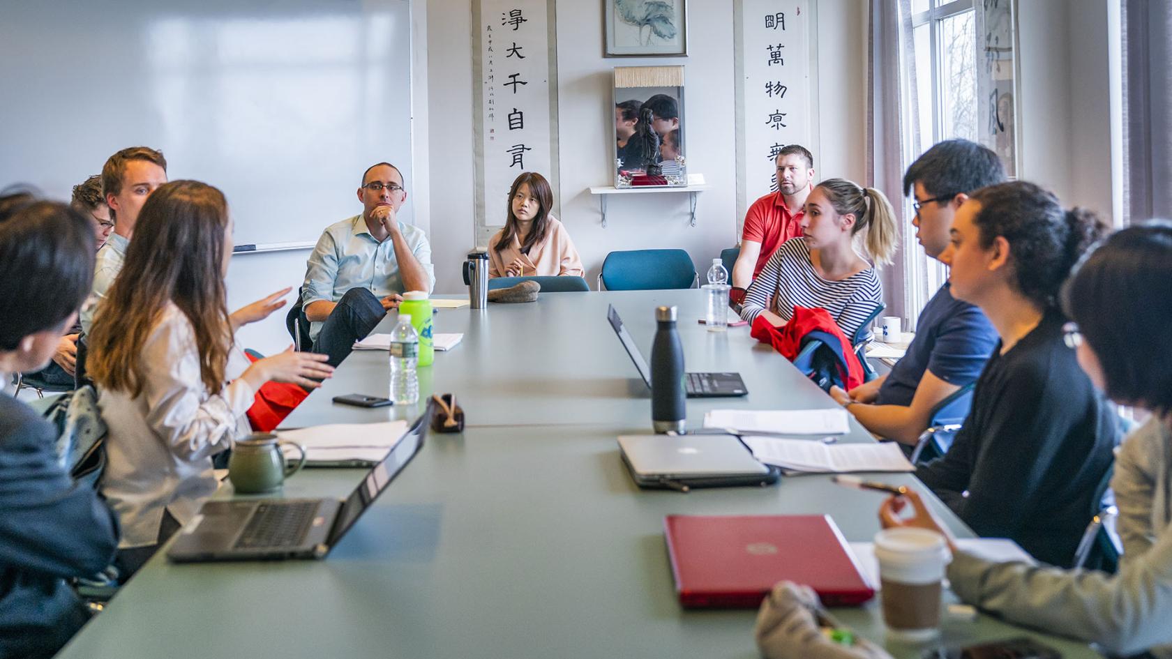 a professor listens to a group of students seated around a table